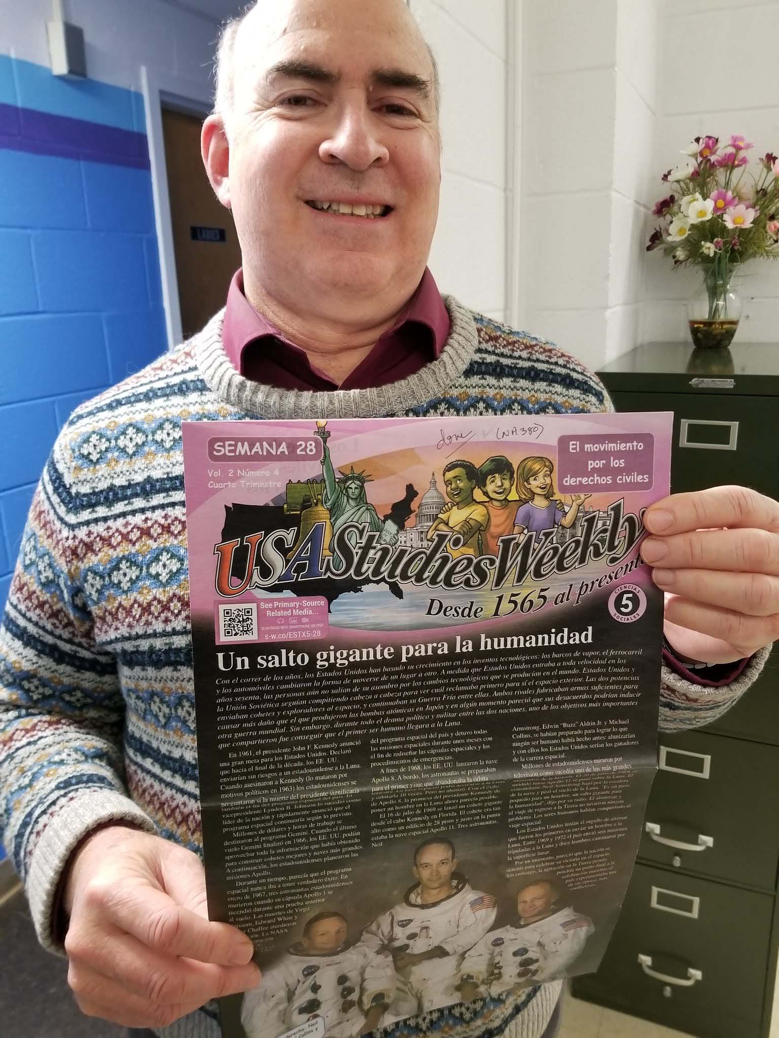 Volunteer David Alper enjoyed reading the Weekly Readers!  In this photo, he is smiling a big smile and holding up a fifth-grade copy about the 1969 moon landing